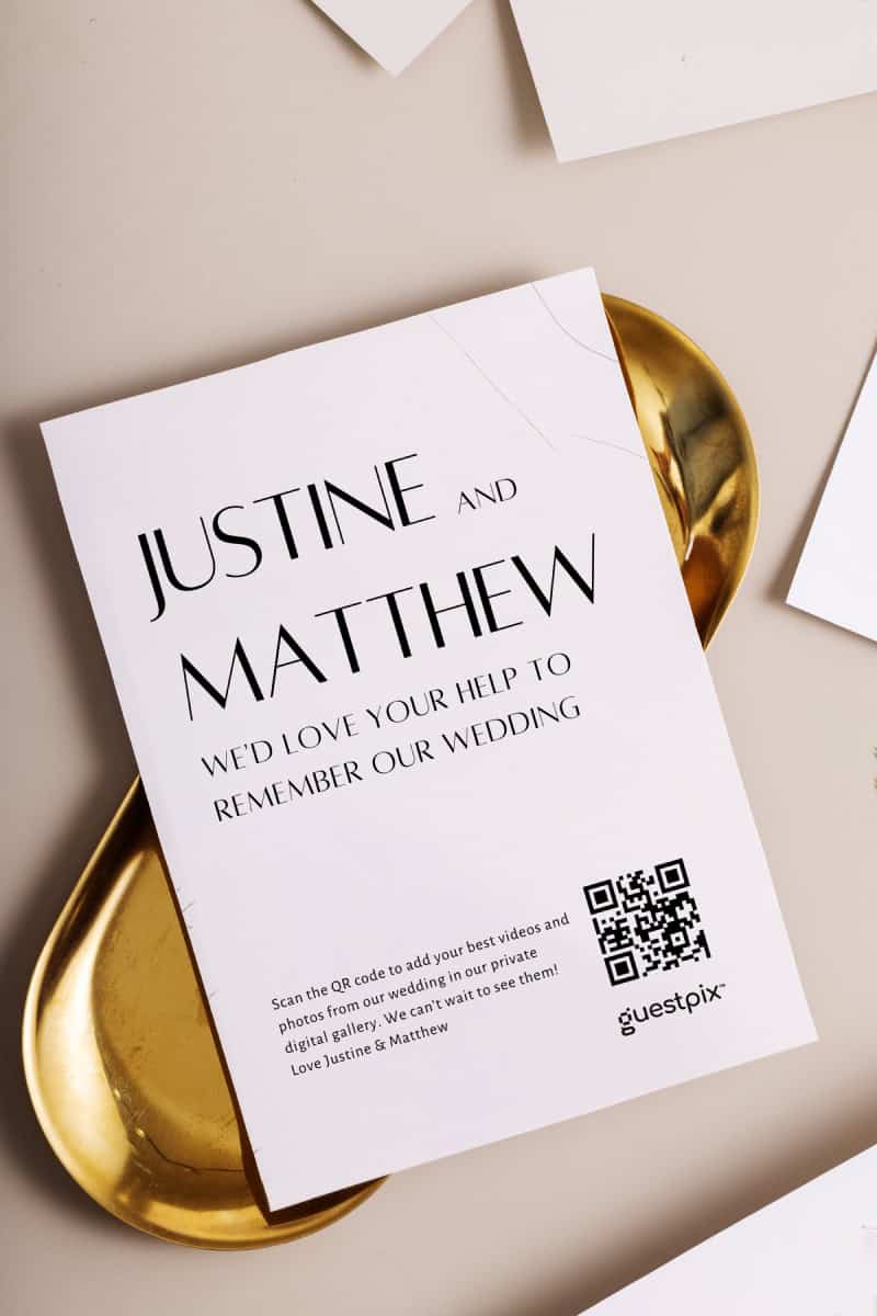 Une invitation de mariage élégante et minimaliste, arborant les prénoms de Justine et Matthew ainsi qu'un code QR permettant d'accéder aux photos de l'événement, le tout sur un fond blanc rehaussé de touches dorées.