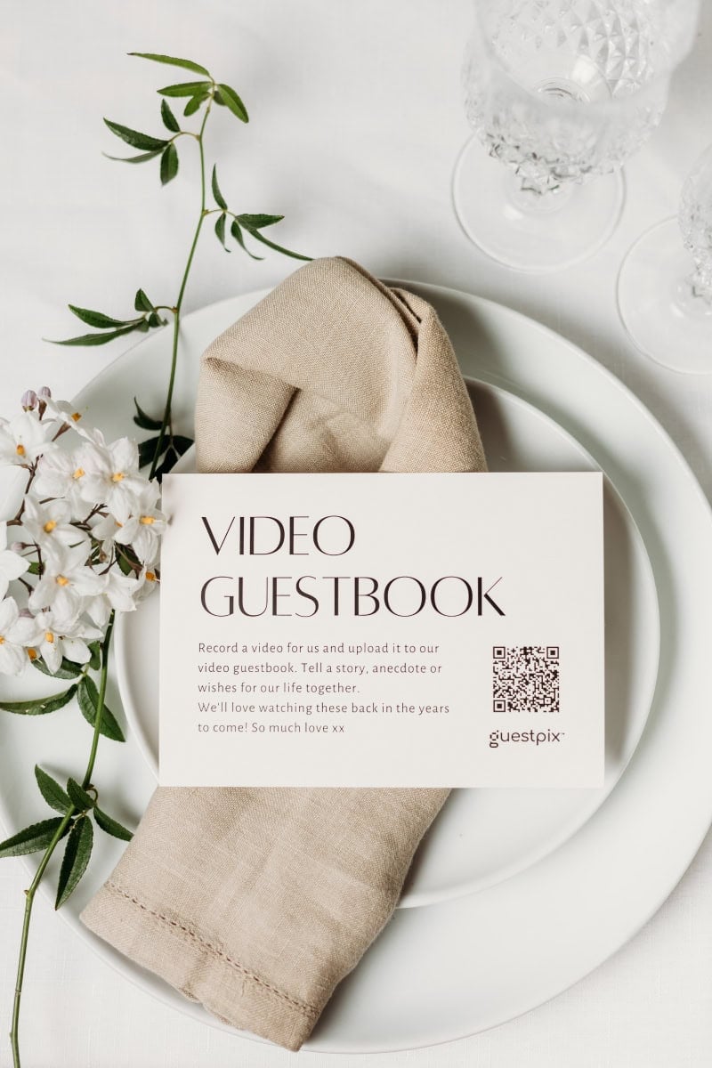 Carte de livre d'or de mariage posée sur une table dressée dans un style minimaliste, avec une serviette beige, une assiette blanche et des touches florales, idéale pour recueillir les souvenirs des invités lors d'un mariage.