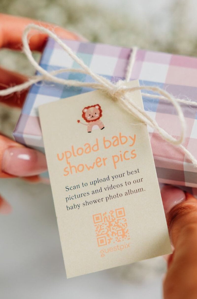 L'immagine di una confezione regalo dai colori pastello con un'etichetta contenente un codice QR per caricare le foto della festa per il nascituro, perfetta per immortalare i momenti speciali della celebrazione.