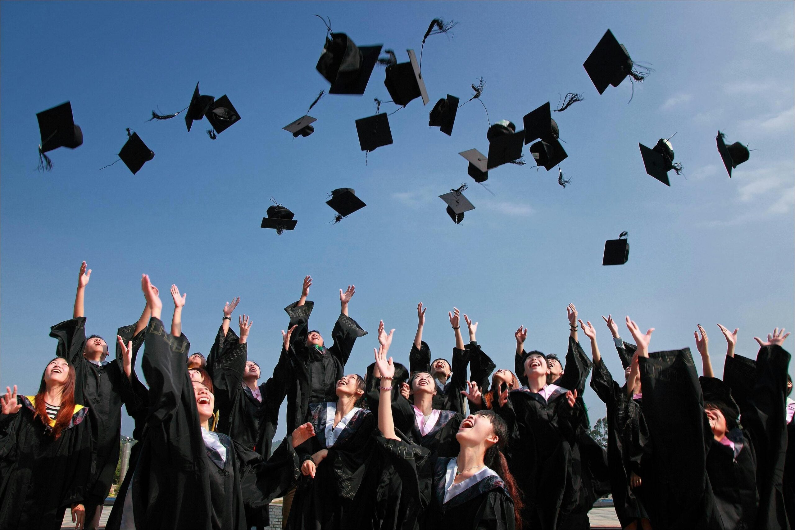 Neolaureati in toga e tocco festeggiano all'aperto mentre lanciano i loro tocchi in aria durante una cerimonia di laurea.