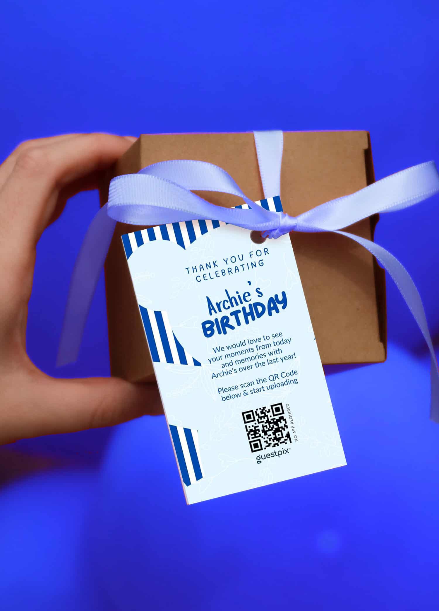 Una mano que sostiene un regalo de cumpleaños envuelto con una etiqueta de agradecimiento en la que aparece un código QR para compartir las fotos del evento, con motivo del cumpleaños de Archie.