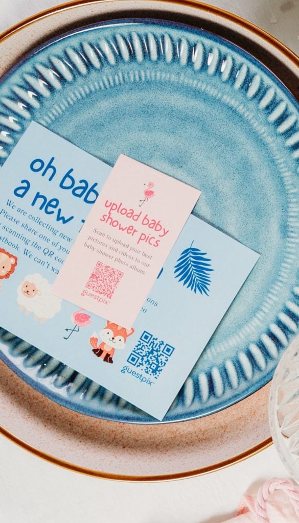 Plato de cerámica azul con invitaciones para una fiesta de bienvenida al bebé y un ramillete de gypsophila blanca sobre una mesa blanca.