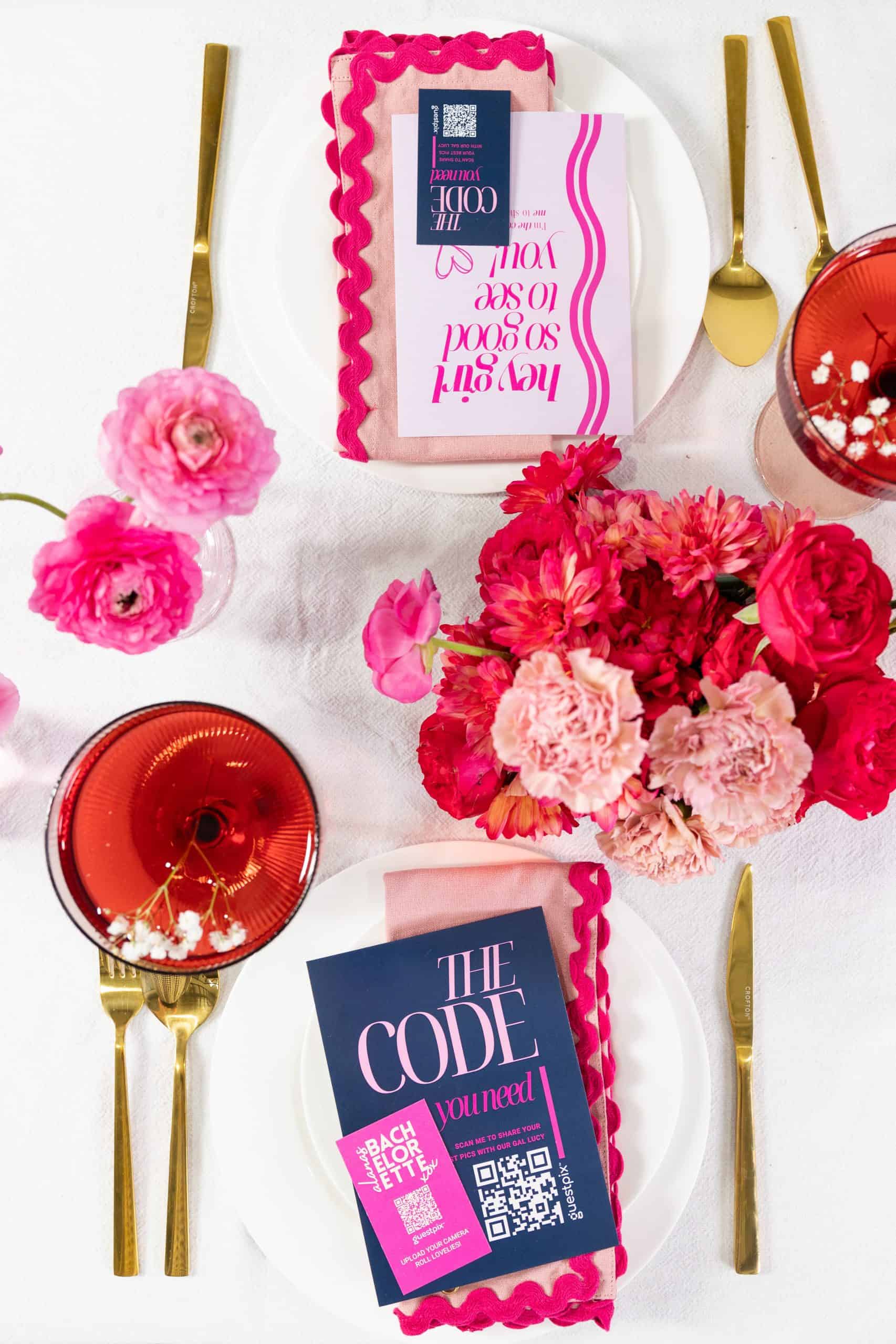 Una tavola apparecchiata a colori con fiori rosa e rossi, posate dorate e inviti all&amp;apos;evento tramite codice QR per una festa o un evento, a promozione della piattaforma di condivisione foto tramite codice QR GUESTPIX.