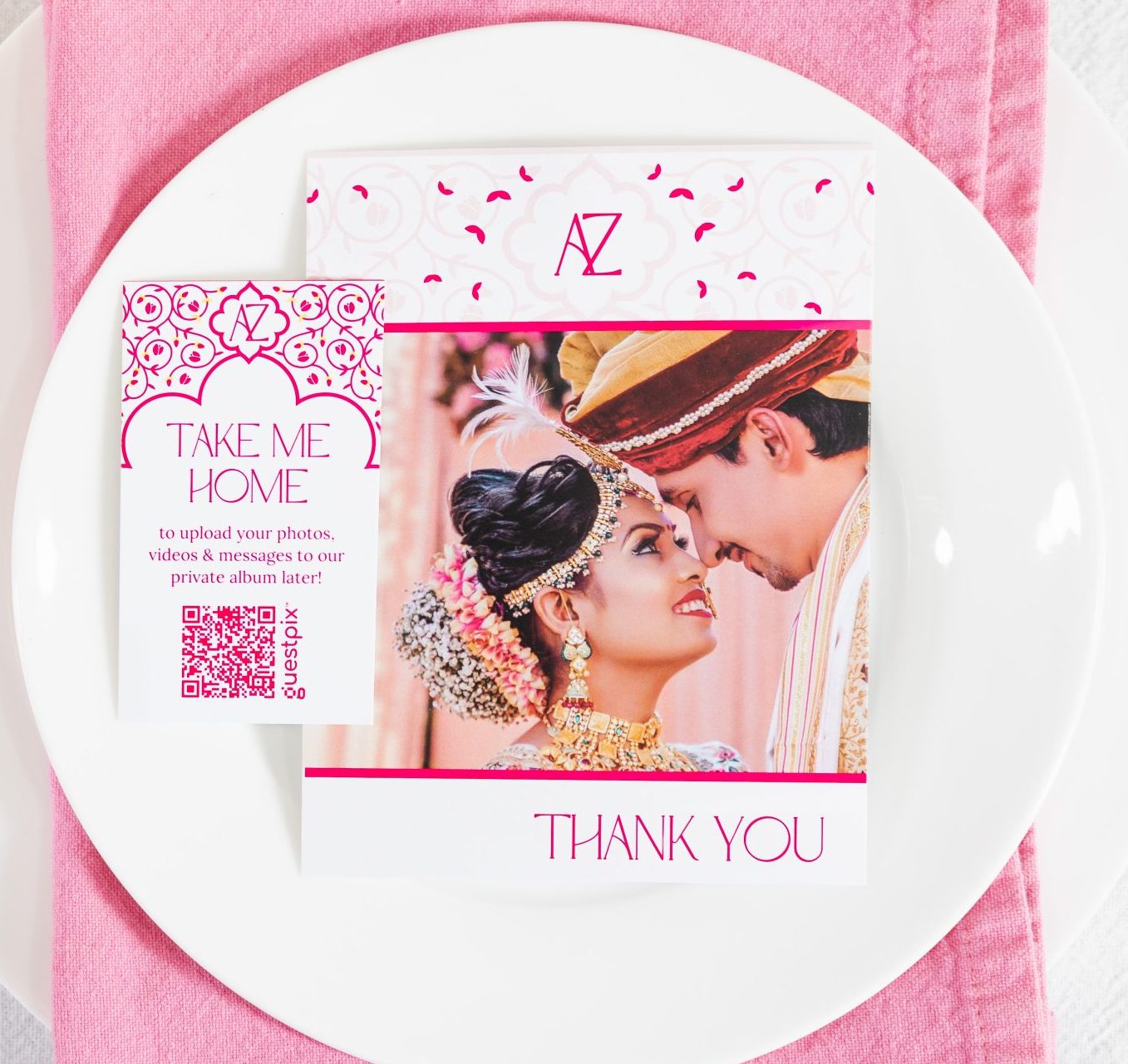 Mesa decorada con motivos nupciales, con una servilleta rosa sobre un plato blanco y cubiertos dorados junto a una tarjeta con un folleto de boda.