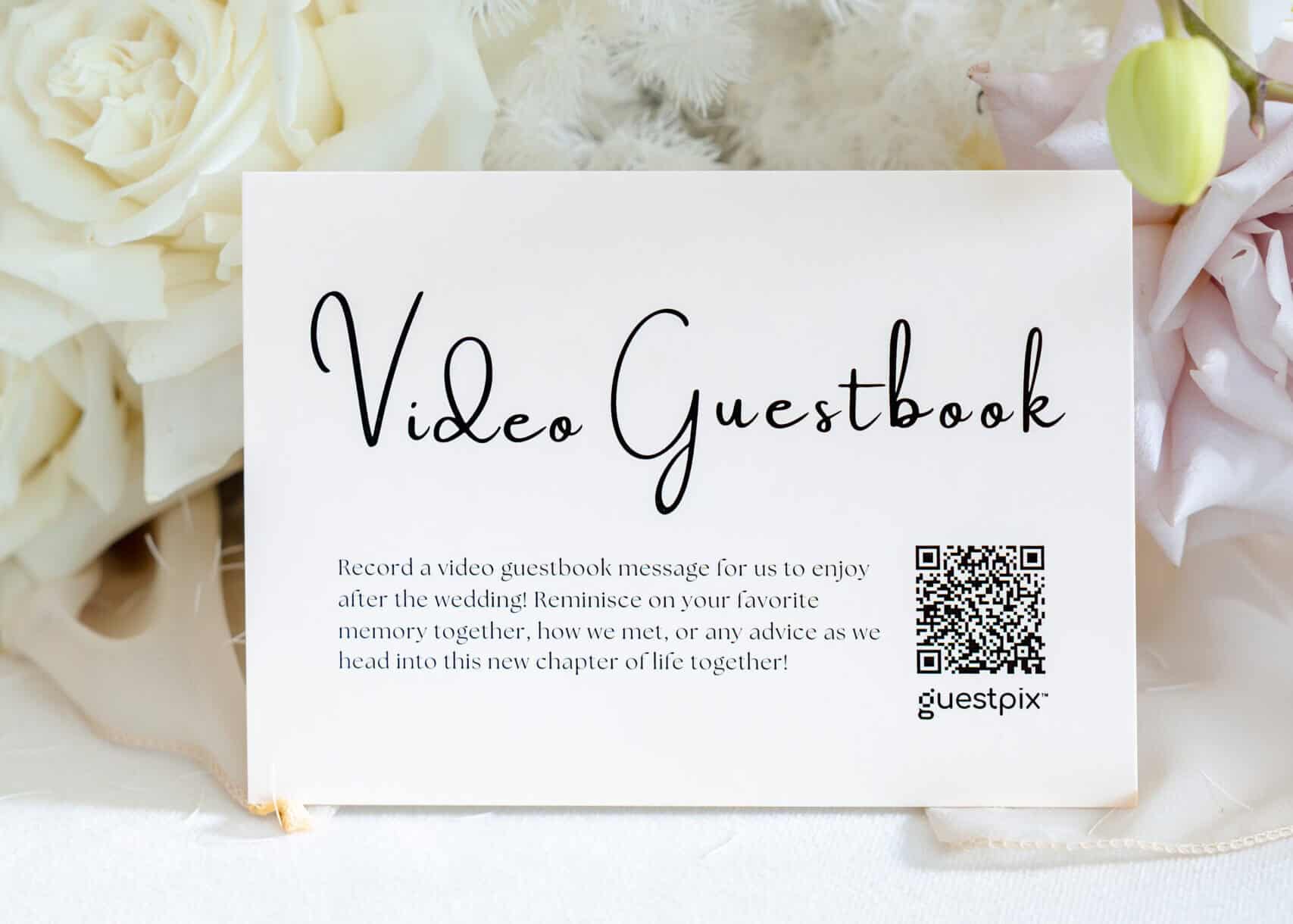 Video Guestbook for Wedding Memories - GUESTPIX | #1 QR Code Event Photo Sharing Platform A wedding video guestbook card with a QR code, surrounded by soft white and blush flowers, inviting guests to record video messages and preserve wedding memories digitally.