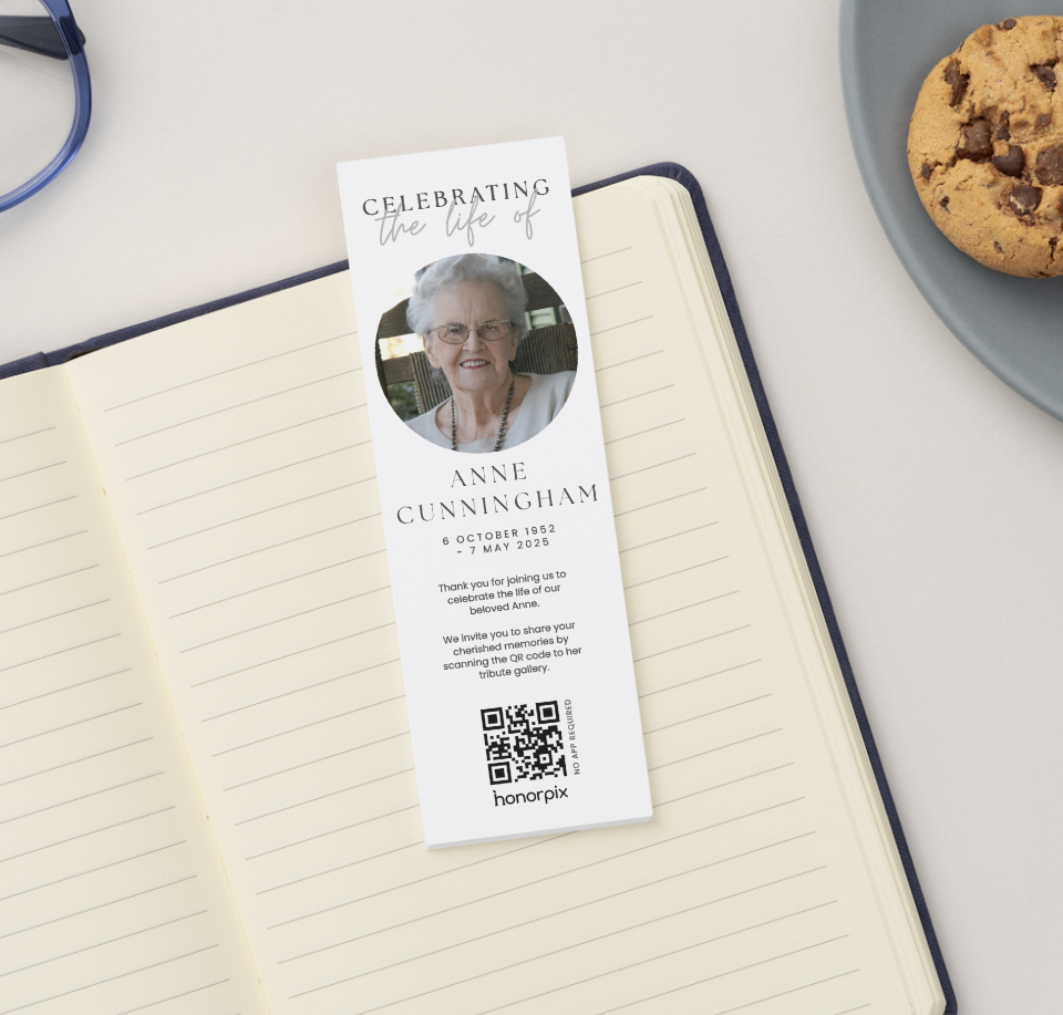 Marque-page commémoratif représentant une photo d'Anne Cunningham, avec l'inscription « En hommage à Anne Cunningham » sur un cahier ouvert, à côté de biscuits et de verres bleus.