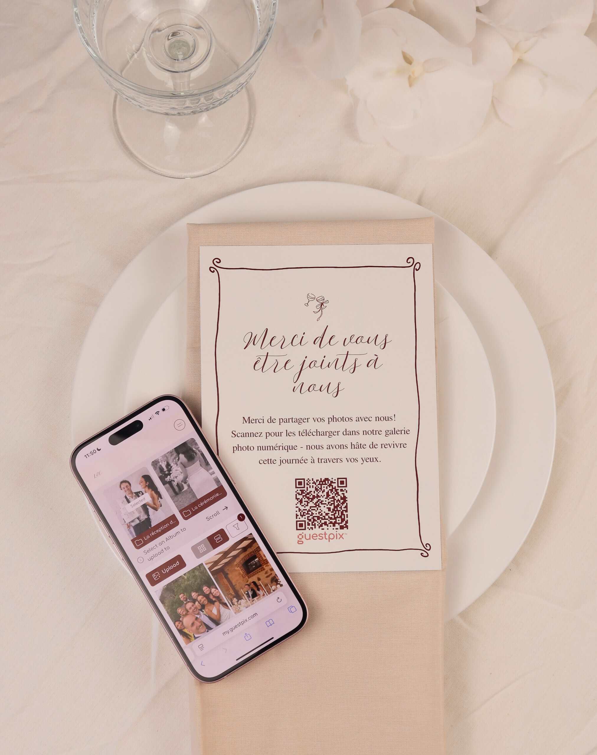 IMG_1703 - GUESTPIX | #1 QR Code Event Photo Sharing Platform Wedding table setting: white plate with beige napkin and a printed card featuring a QR code, plus a glass and a smartphone displaying photos on a light tablecloth.