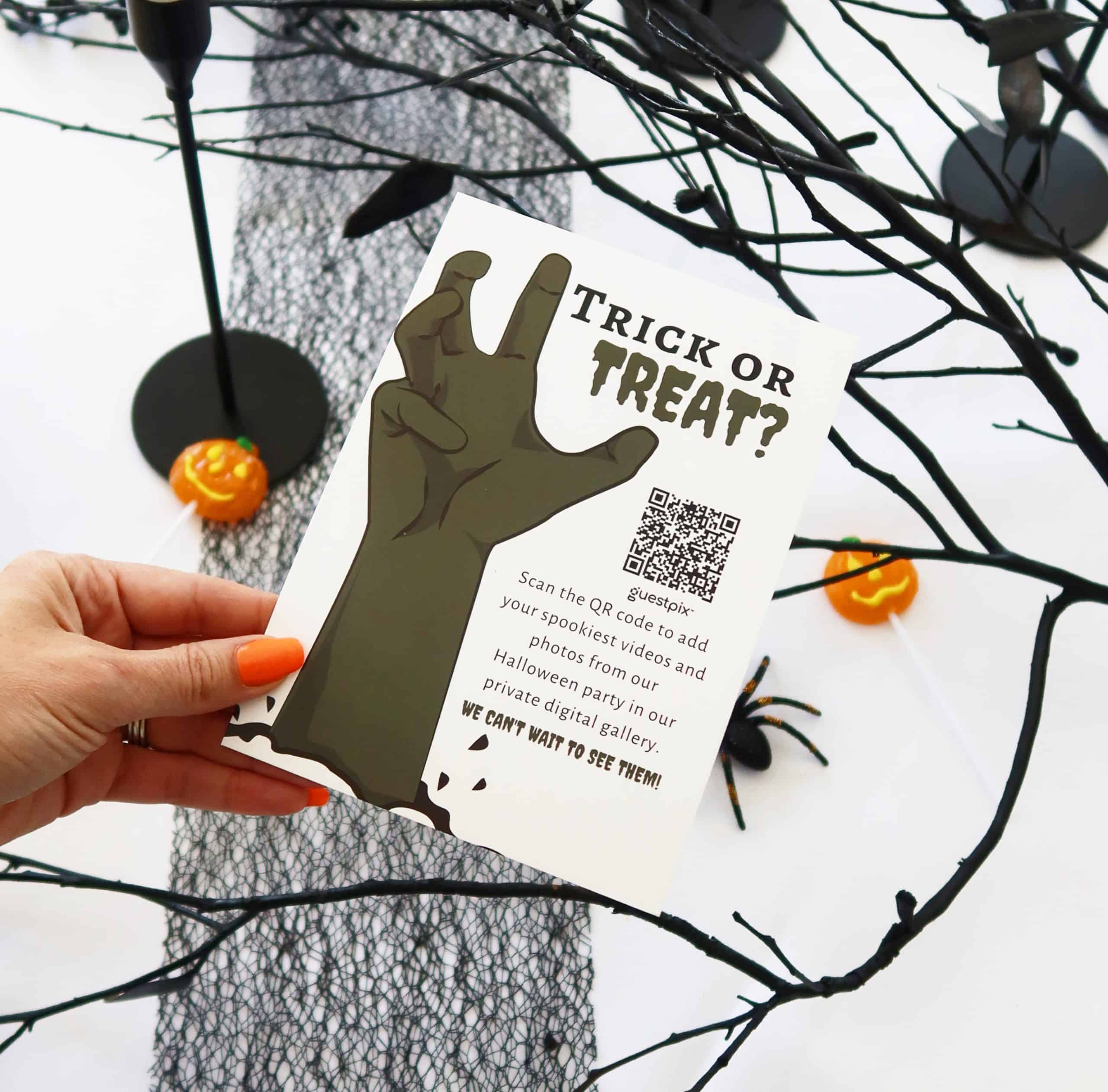 「トリック・オア・トリート？」と書かれたQRコード付きのハロウィーンのチラシを手にした手が写っており、画面の外には黒い枝やキャンディのカボチャが散りばめられている。