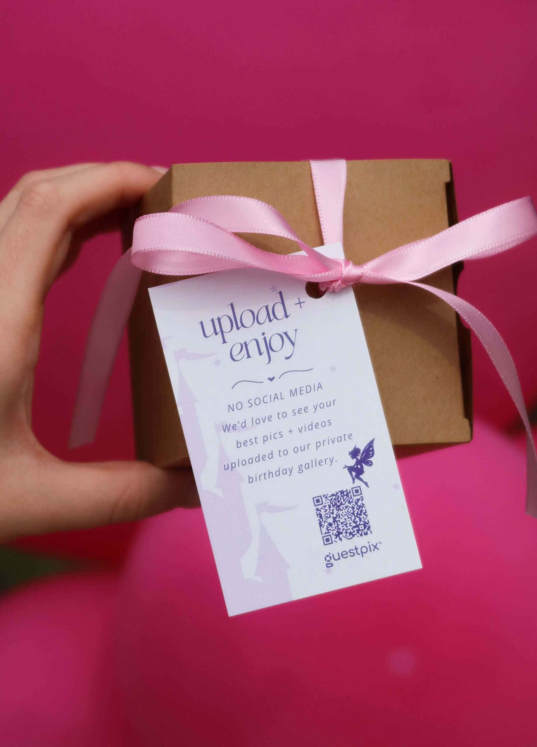 Caja de regalo con código QR para una fiesta de cumpleaños infantil, decorada con un lazo rosa, que promociona la plataforma de intercambio de fotos de eventos GUESTPIX.