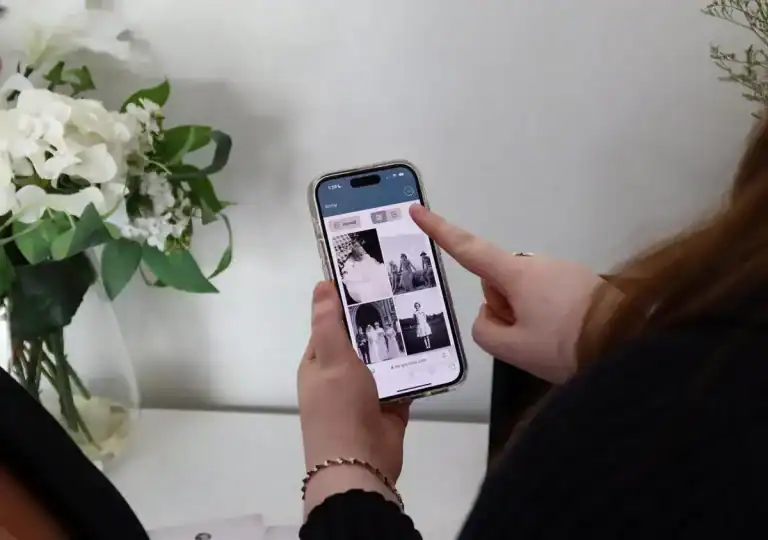 Person holding a smartphone and viewing a grid of black-and-white photos, with white flowers in the background.