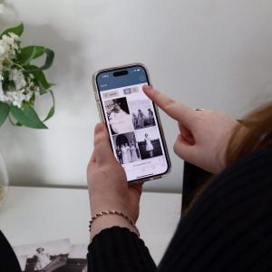 Eine Person, die ein Smartphone in der Hand hält, auf dessen Bildschirm ein Raster aus Schwarz-Weiß-Fotos zu sehen ist.