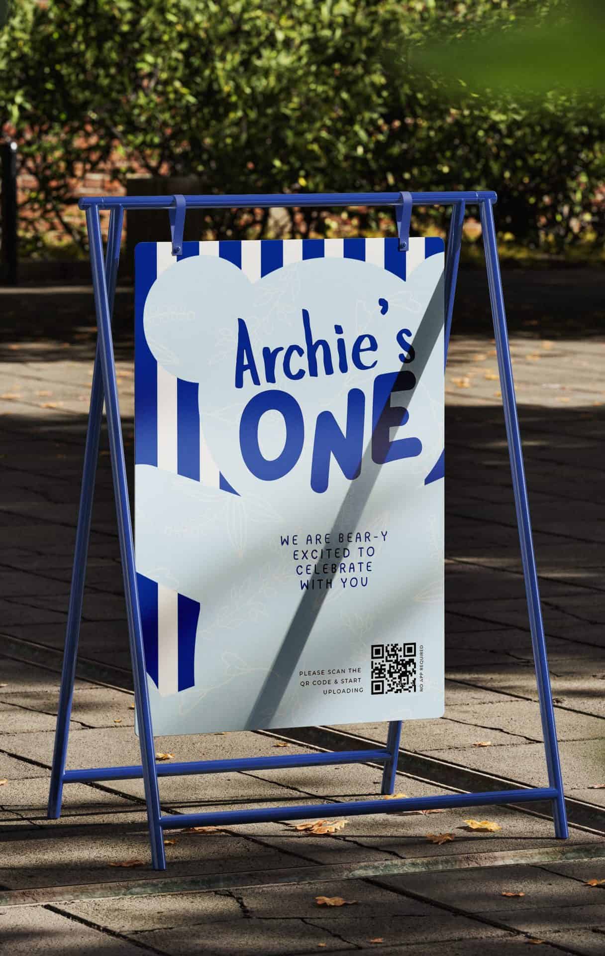 Un colorido cartel exterior para celebrar el primer cumpleaños de Archie, con rayas azules y blancas, globos y un código QR con las fotos del evento.