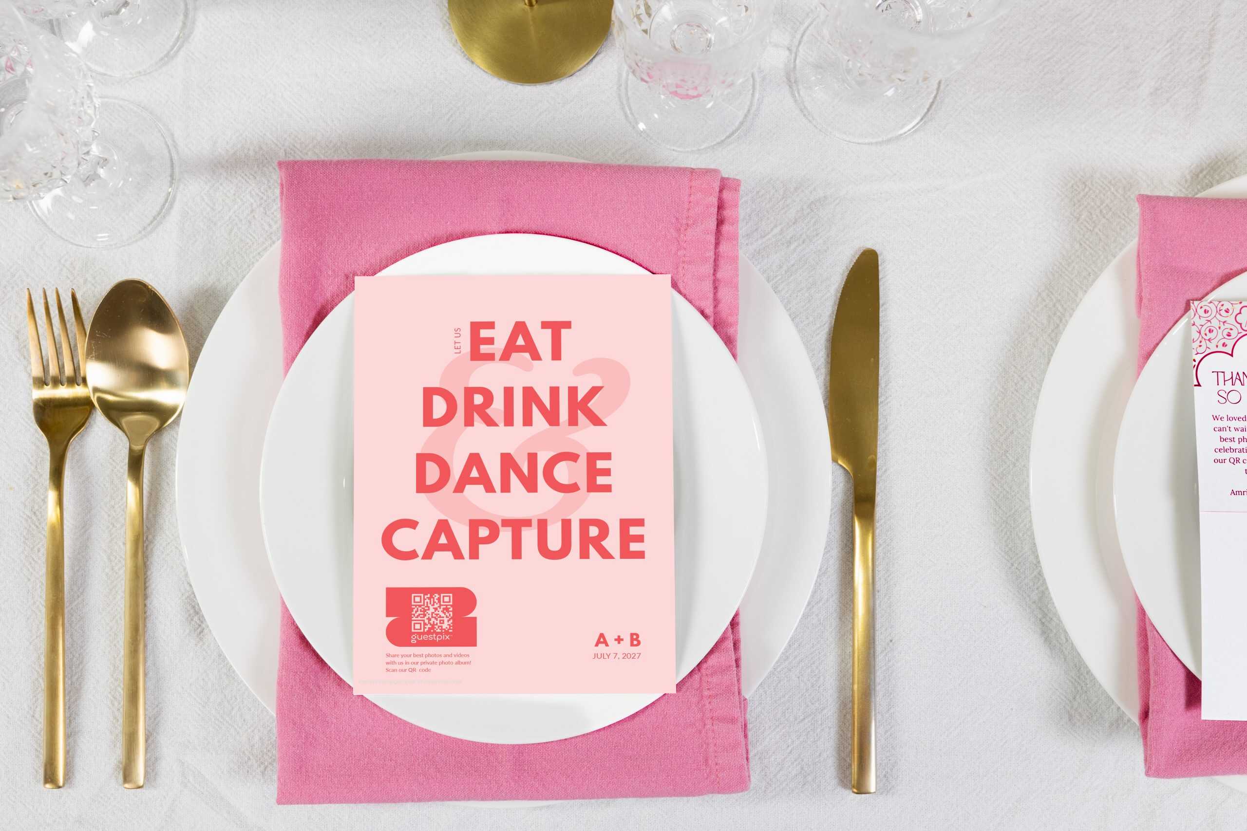 Una colorida tarjeta de menú para eventos con las palabras «Come, bebe, baila, captura» y un código QR, colocada sobre un plato blanco con una servilleta rosa, cubiertos dorados y cristalería.