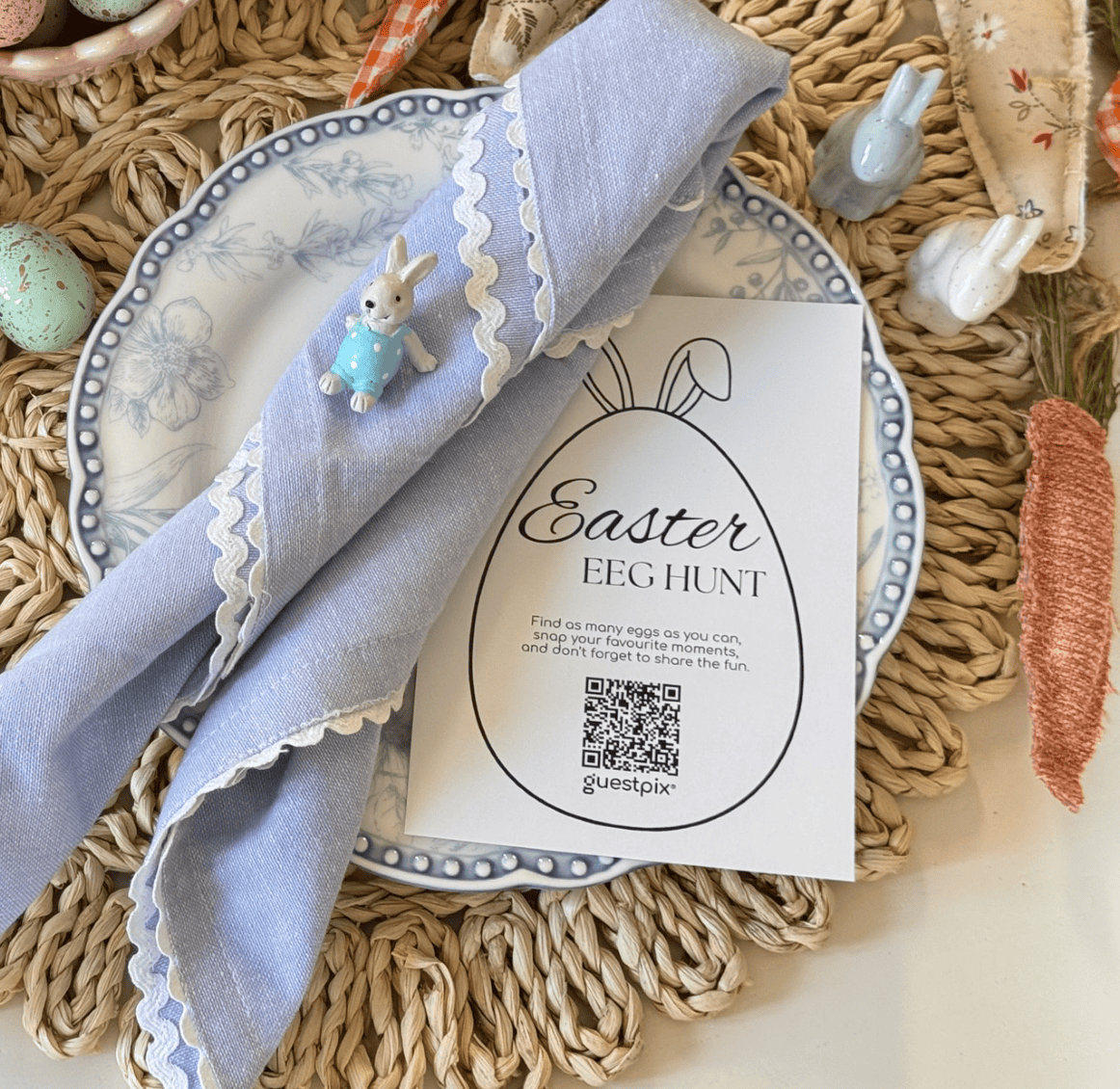 Huevos de Pascua con motas en tonos pastel dispuestos sobre un mantel individual tejido, junto a un plato con borde azul y una servilleta cuidadosamente doblada.