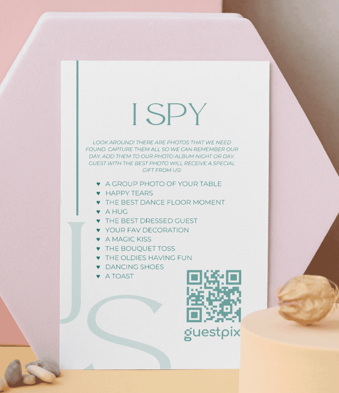 Posterkarte mit dem Titel „I SPY“ mit einer Schnitzeljagd-Liste und einem QR-Code für „Guestpix“ vor einem pastellrosa Hintergrund.