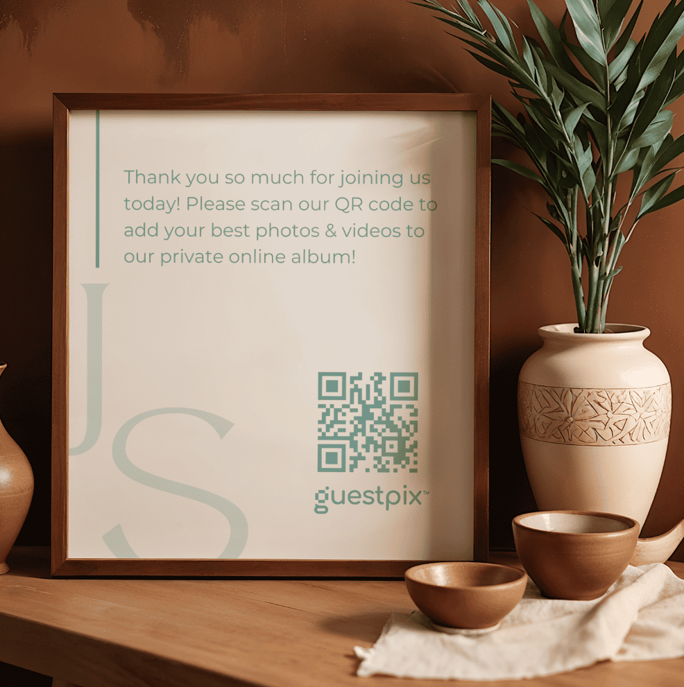 Gerahmtes Schild mit einem QR-Code zum Hochladen von Fotos in ein privates Online-Album; daneben eine Pflanze und Keramikschalen.