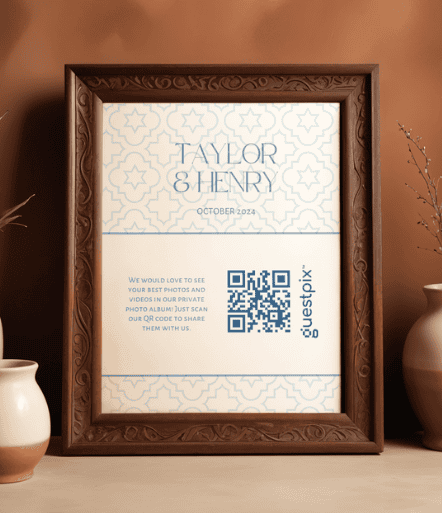 Un marco de madera ornamentado, colgado en una pared de tonos cálidos, sostiene un cartel de «Taylor &amp; Henry, octubre de 2024», con un código QR para que los invitados suban sus fotos.
