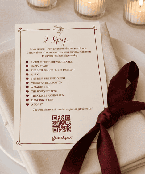 Une carte intitulée « I Spy... » proposant des indices sous forme de photos pour une chasse au trésor, posée sur une serviette nouée d'un ruban bordeaux ; des bougies brillent en arrière-plan.