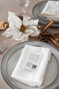 Gros plan sur une table de mariage raffinée, avec une serviette blanche ornée d'un code QR, posée sur une assiette grise agrémentée d'éléments décoratifs naturels, idéale pour les mariages au style minimaliste et moderne.