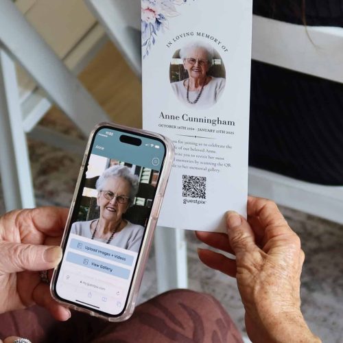 Elderly woman scanning a memorial QR code on a printed tribute card with her smartphone at a memorial event.