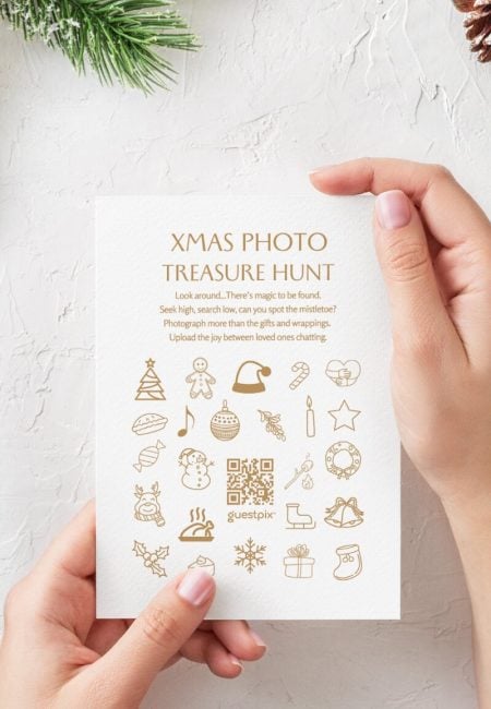 A person holding a holiday-themed treasure hunt card with Christmas icons and a QR code, promoting festive photo sharing at an event.
