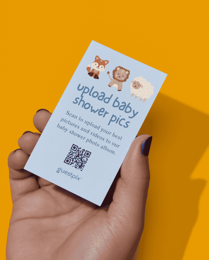 Une carte portant la mention « Téléchargez les photos de la fête prénatale » et comportant un code QR, tenue dans une main sur fond orange ; invite à télécharger les photos de la fête prénatale.