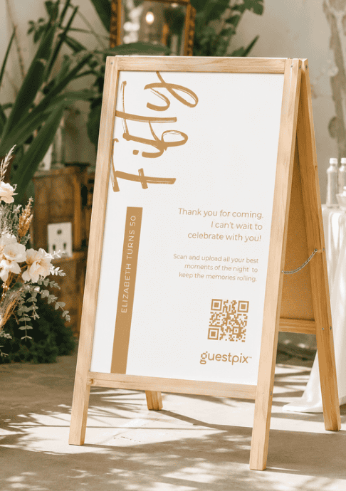 Cartel de madera con estructura en forma de A y un póster blanco en el que se ve una cinta con el mensaje «Elizabeth cumple 50», un mensaje de cumpleaños y un código QR, para uso en exteriores.