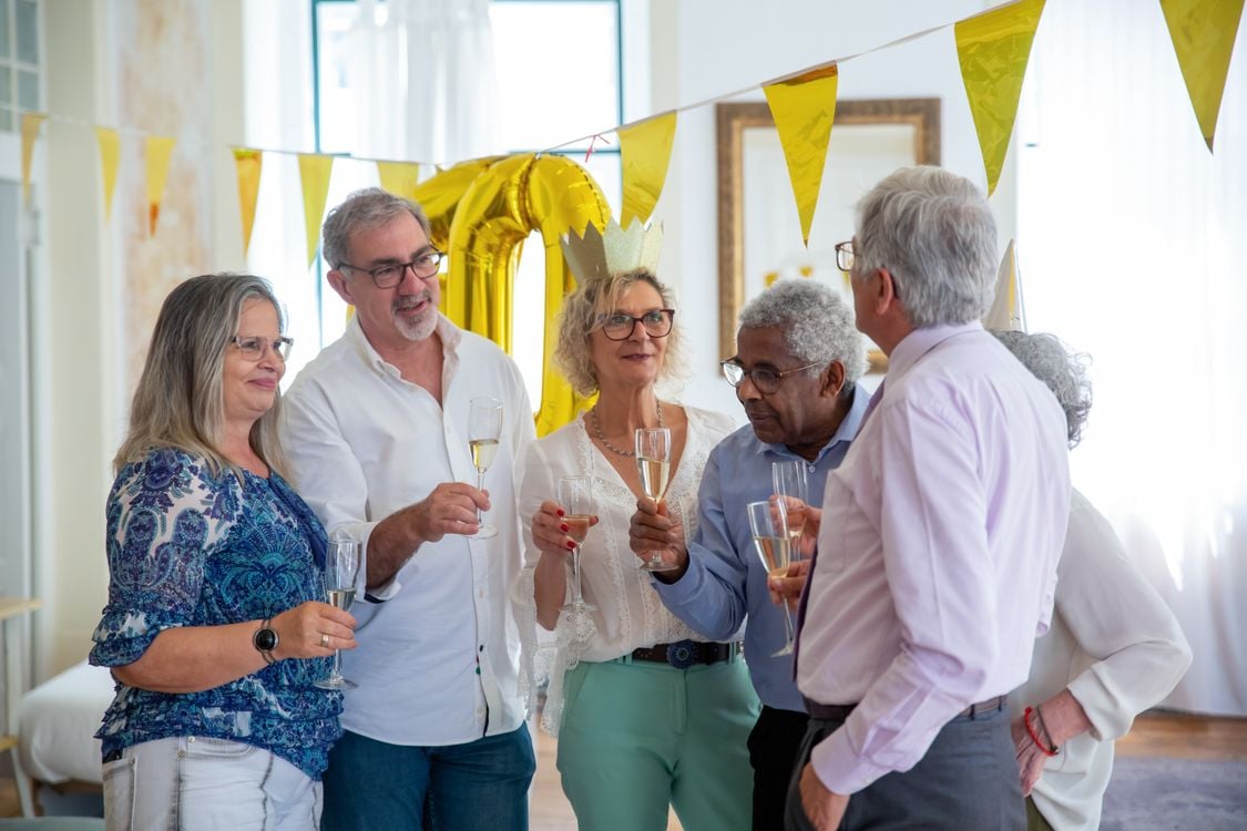 Un groupe d'amis d'âge mûr, tout sourire, célébrant un 60e anniversaire avec des coupes de champagne et des sourires