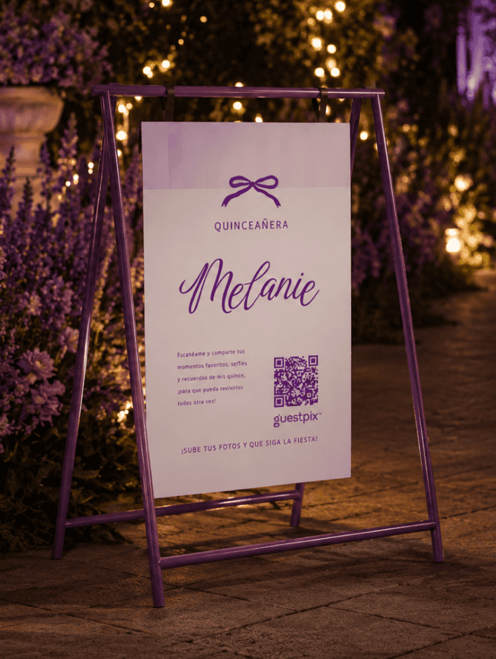 Cartel del evento con marco morado para la quinceañera de Melanie, con un icono de un lazo y un código QR, iluminado por cálidas luces de jardín.