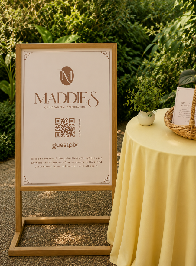 Insegna in legno per la Quinceañera di Maddie con un codice QR, posizionata accanto a un tavolo apparecchiato con una tovaglia gialla e a un cesto di vimini contenente i menu.