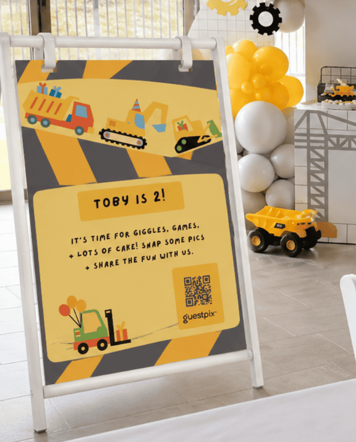 「トビー、2歳！」と書かれた、建設現場をテーマにしたポスター。誕生日パーティーを舞台に、黄色と灰色のストライプを背景におもちゃのトラックやショベルカーが描かれている。