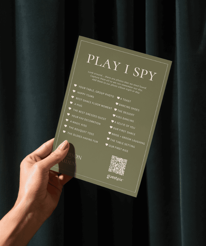 Una mano che regge una scheda verde dell'attività "Play I Spy" con un elenco di spunti fotografici per un matrimonio o un evento.