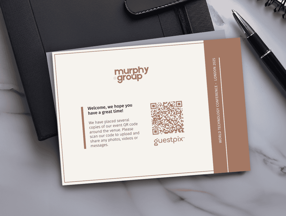 Veranstaltungsbroschüre auf einem Schreibtisch mit dem Logo der Murphy Group, einer Begrüßungsbotschaft, einem QR-Code und dem „Guestpix“-Branding.