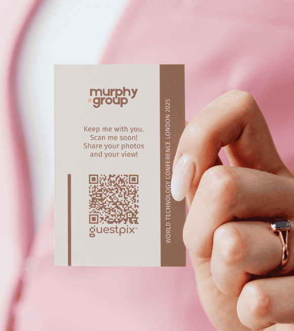 Una mano que sostiene una tarjeta de congresos de color beige con el logotipo de Murphy Group, un código QR y el texto «World Technology Conference London 2025» escrito verticalmente sobre una franja marrón.