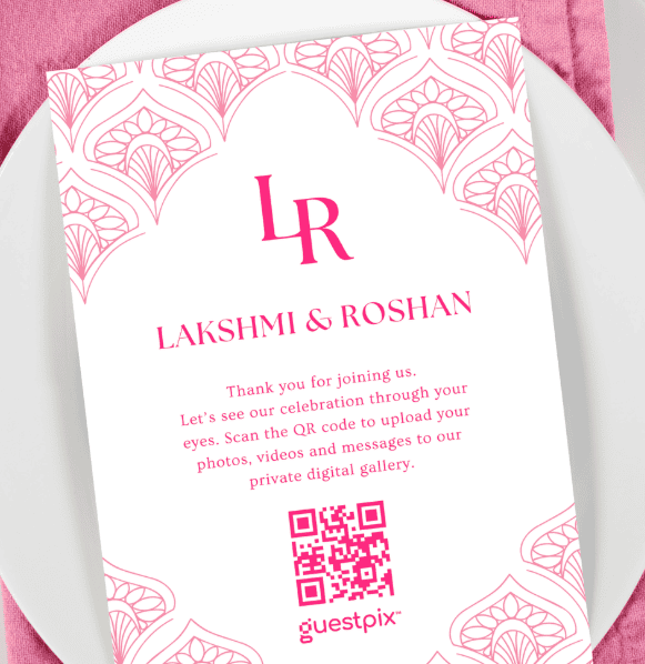 Weiße Hochzeitseinladungskarte mit rosa Zierrand, dem Monogramm „LR“, den Namen „Lakshmi &amp; Roshan“ und einem QR-Code für die private Galerie (guestpix).