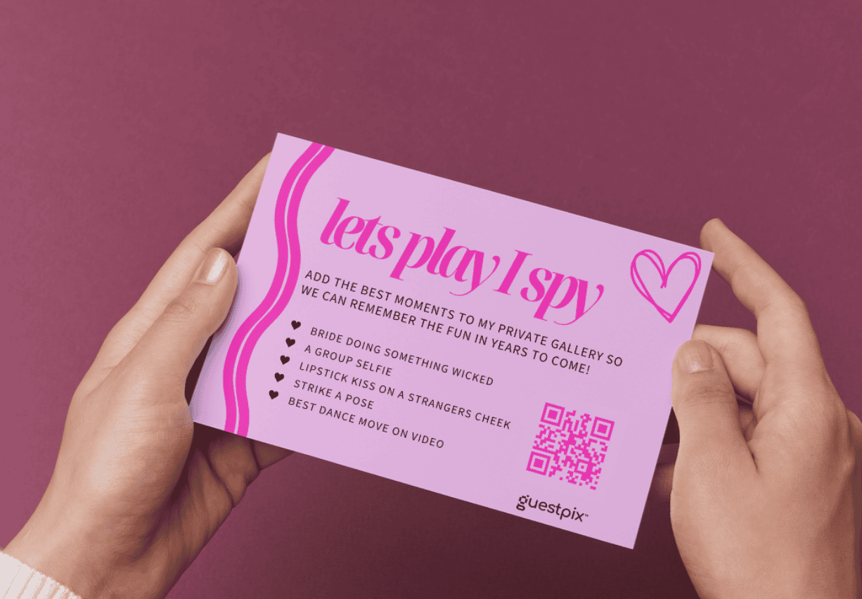 Biglietto rosa per l'evento intitolato "Giochiamo a 'Trova l'oggetto'", tenuto tra due mani, con l'immagine di un cuore e un codice QR sul lato destro.