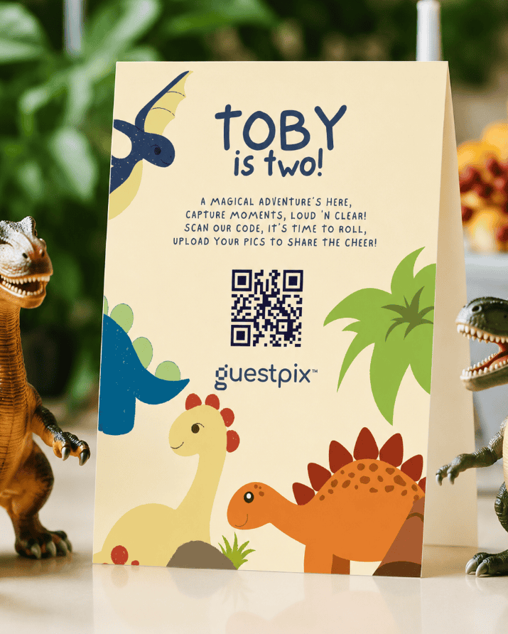 Vertikales Poster mit der Aufschrift „TOBY wird zwei!“ mit bunten Dinosaurier-Illustrationen und einem QR-Code für eine Schnitzeljagd bzw. eine Mitmachaktion auf der Party