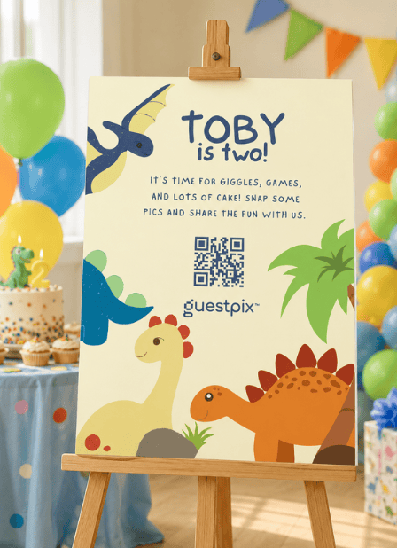 Geburtstagsschild auf einer Staffelei mit der Aufschrift „Toby ist zwei!“ sowie bunten Dinosaurier-Illustrationen und Luftballons.