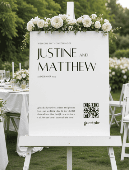 Cartello di benvenuto per un matrimonio su un cavalletto con una ghirlanda di fiori, su cui sono riportati i nomi “Justine e Matthew” e la data “22 dicembre 2025”, in occasione di un ricevimento all’aperto.