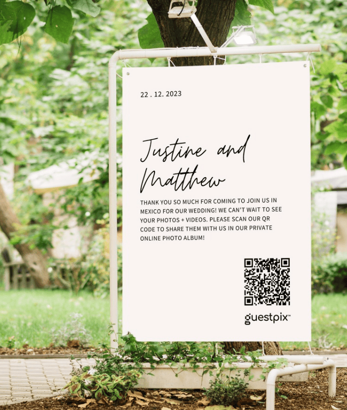 Hochzeitsschild mit der Aufschrift „Justine und Matthew“, dem Datum 22.12.2023 und einem QR-Code zum Teilen von Fotos, aufgestellt im Freien.