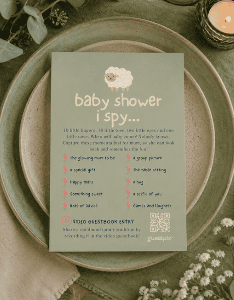 Blaugrüne „Ich sehe, was du nicht siehst“-Spielkarte für eine Babyparty auf Keramiktellern, umgeben von Grünpflanzen und einer brennenden Kerze.