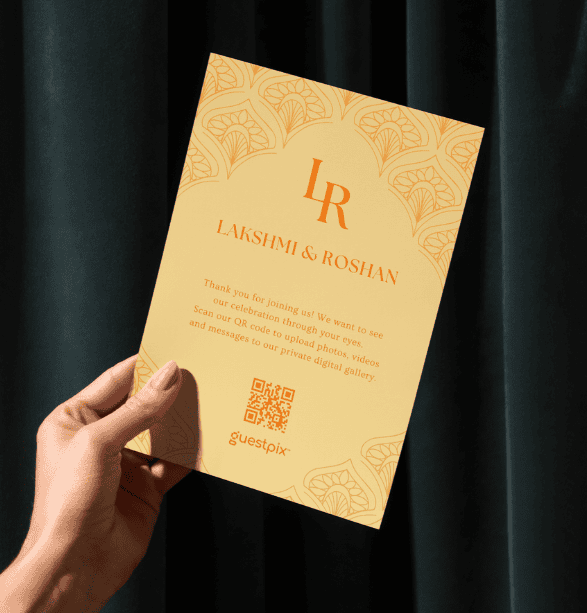 Invitación de boda en tono naranja pastel con un borde ornamentado, las iniciales «LR» y los nombres «Lakshmi» y «Roshan», sostenida por una mano con un código QR en la parte inferior