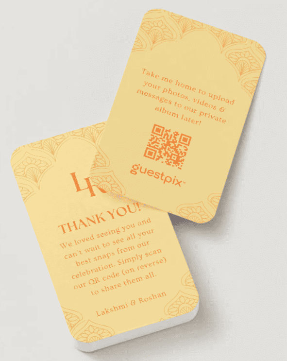 Dos tarjetas de invitación de color amarillo pálido con bordes decorativos; una de ellas incluye un código QR y el logotipo de Guestpix para compartir fotos.